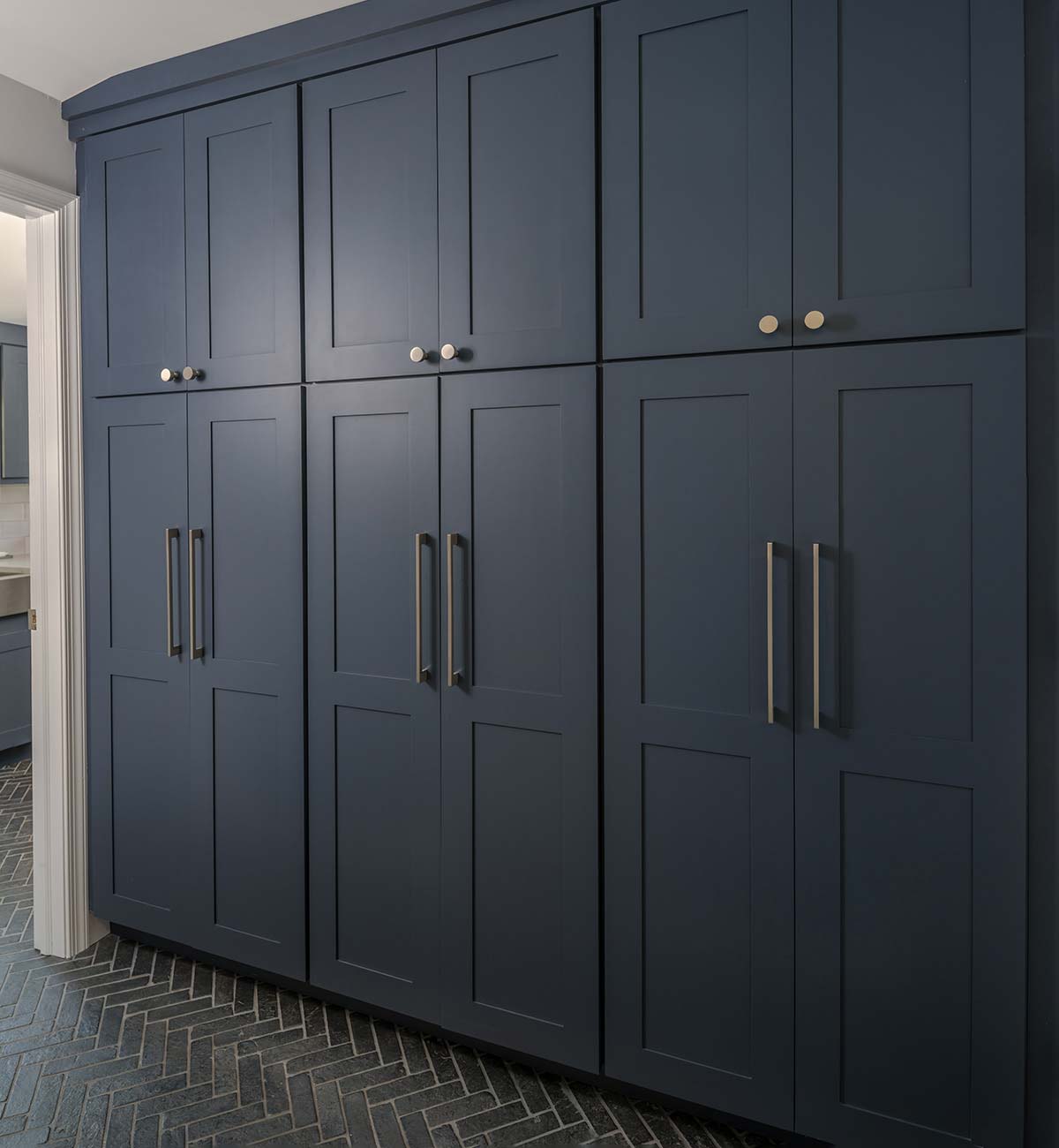 Tall dark blue cabinets with brass handles in a room with a black herringbone tile floor.
