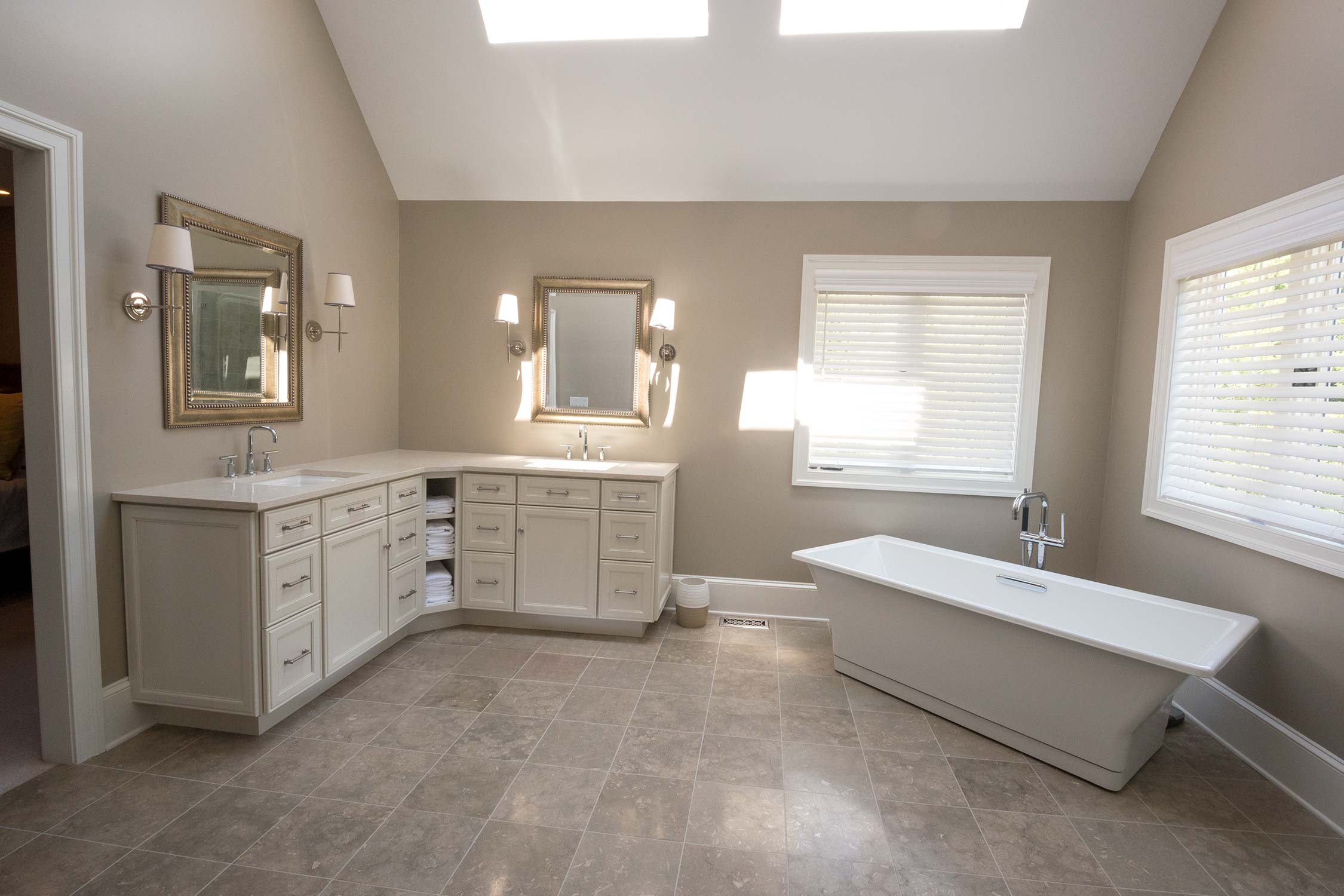 Spacious bathroom with dual vanities, freestanding tub, skylights, large mirrors, and tiled flooring with natural light.