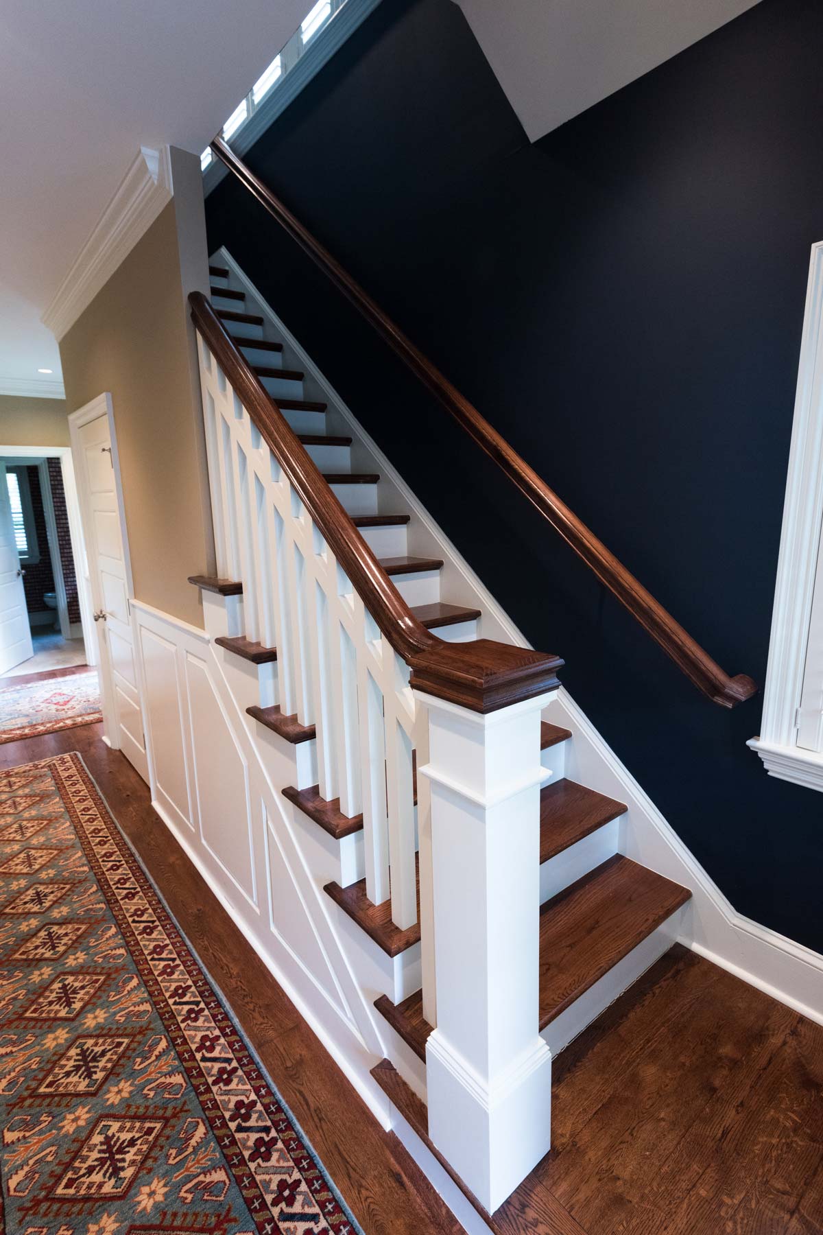Elegant staircase with dark wood steps, white railings, and a deep blue wall, complemented by a vibrant rug and hardwood flooring.