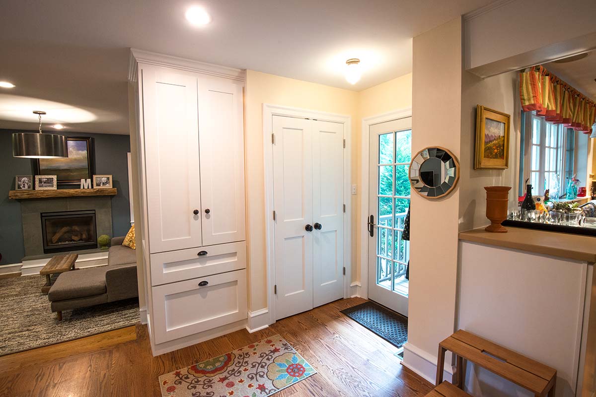 Welcoming entryway with white cabinets, glass door, and vibrant rug, leading to a cozy living area with fireplace and modern decor.
