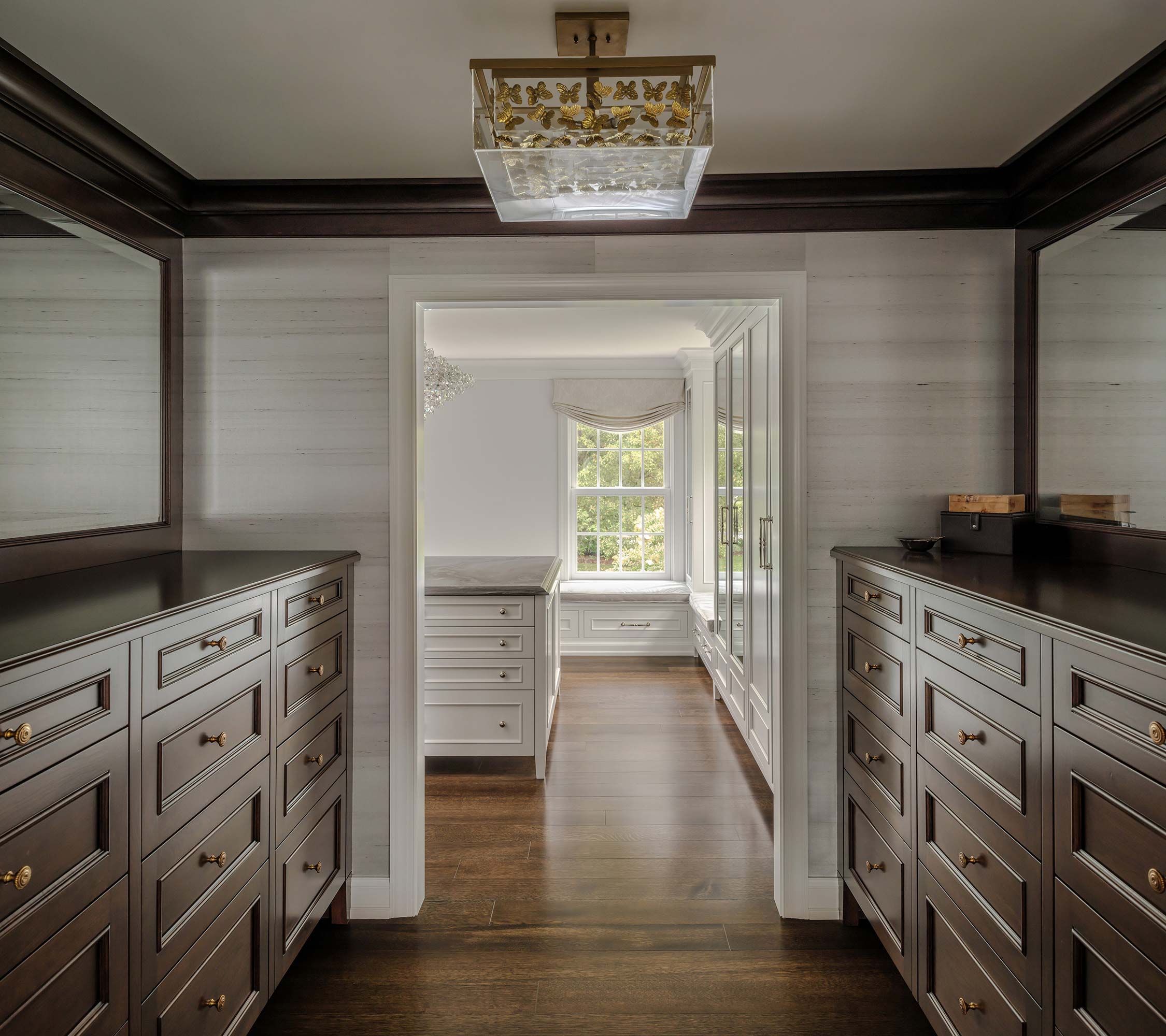 Stylish dressing room with dark wood cabinets, marble countertops, a decorative chandelier, and large windows with a green view.