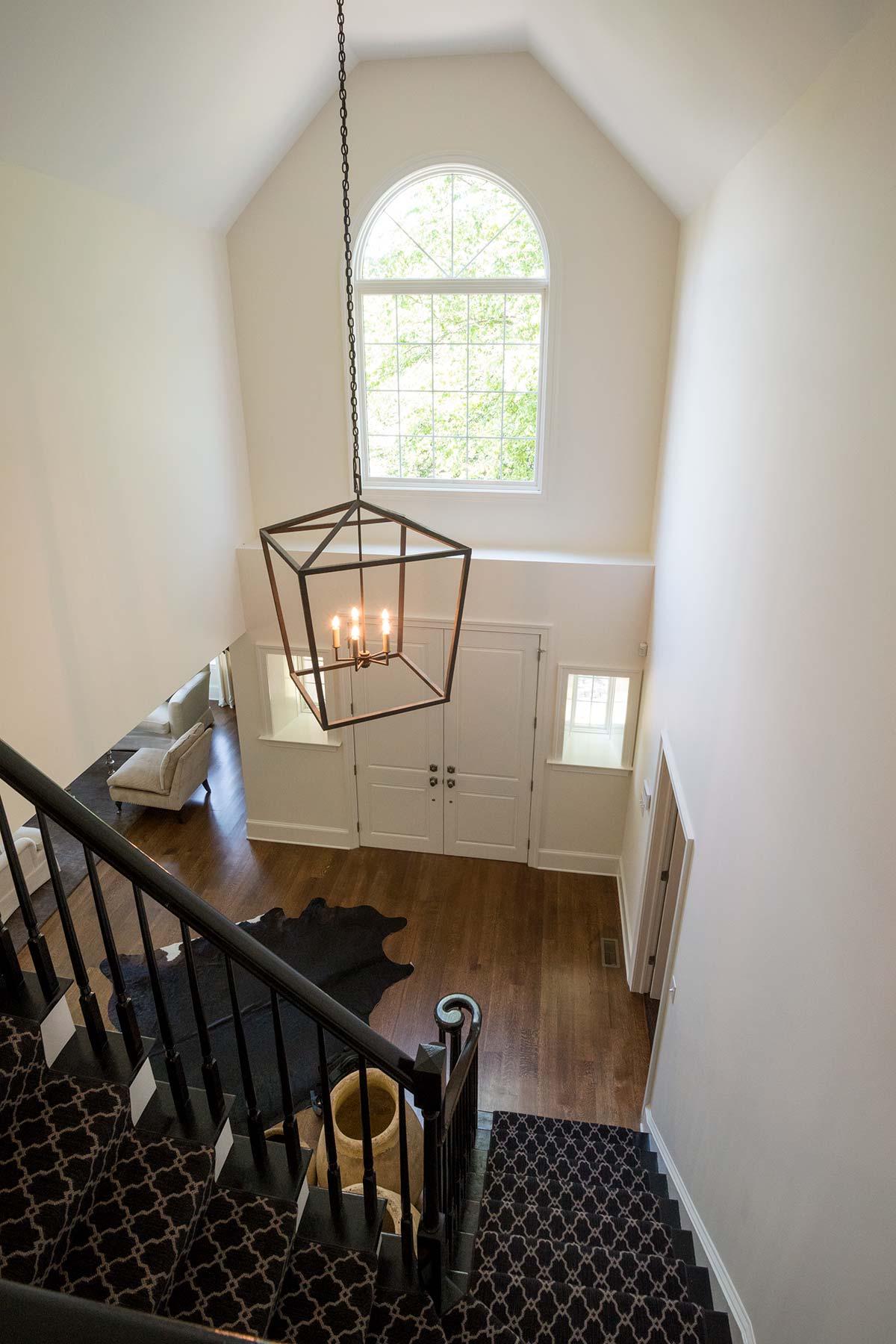 Elegant foyer with a grand staircase, modern chandelier, large arched window, and a cowhide rug on hardwood flooring.
