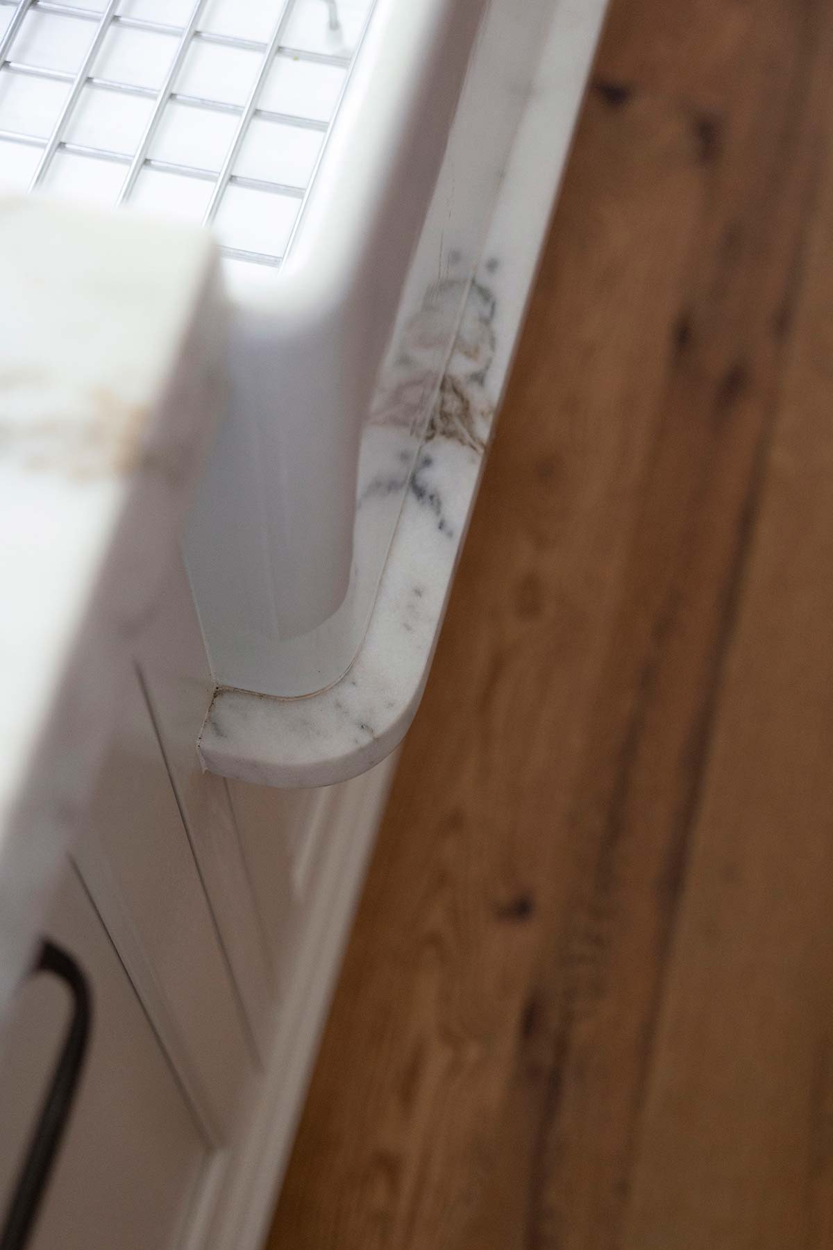 Close-up of a white farmhouse sink with a marble countertop, set against rustic wooden flooring, showcasing elegant kitchen design.