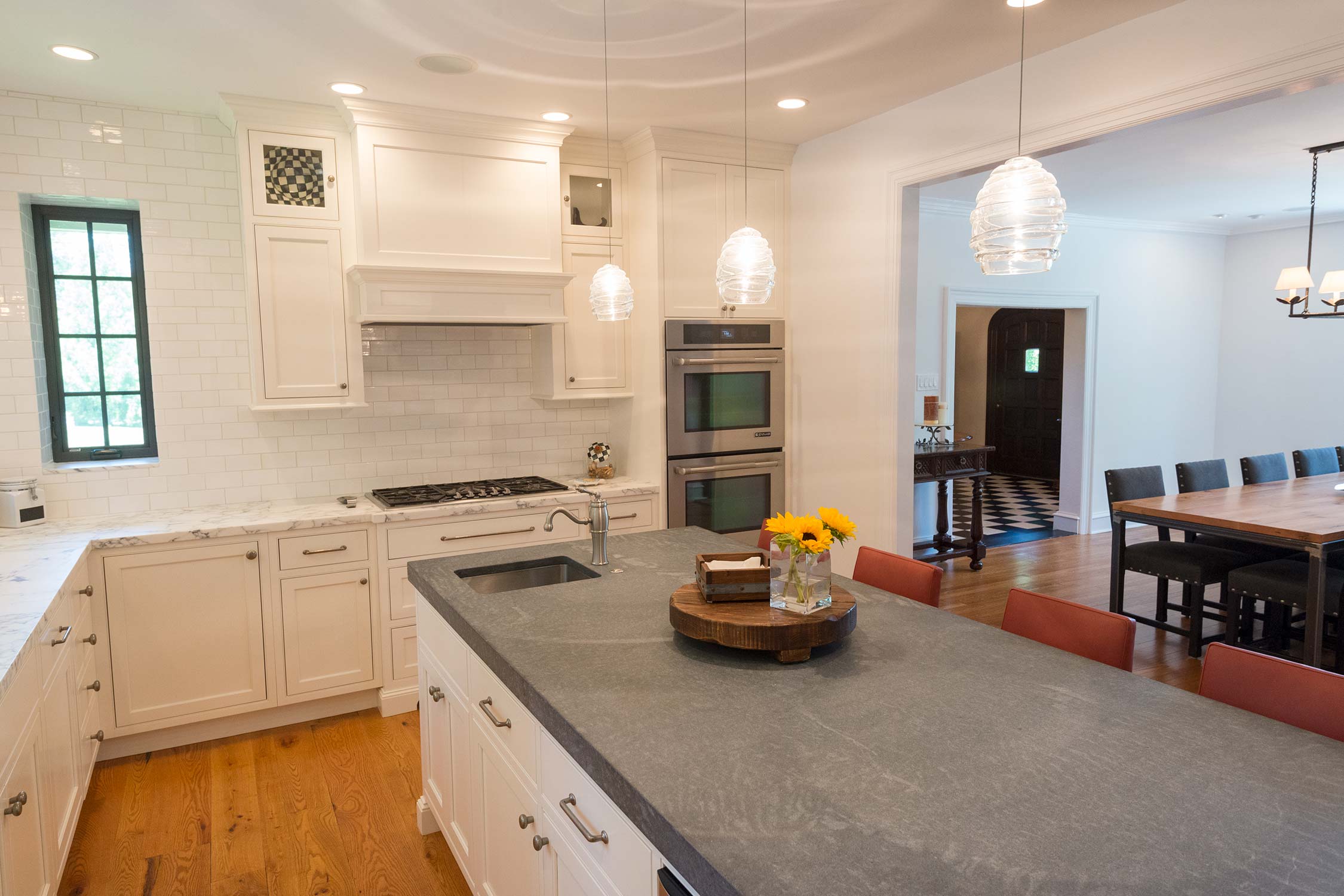Bright kitchen with white cabinets, gray stone island, pendant lights, and a view into a stylish dining area.