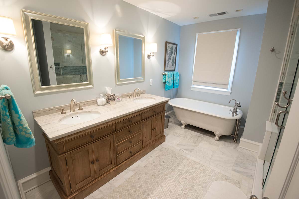 Elegant bathroom with dual vanity, marble countertop, and a classic clawfoot tub. Soft blue accents and bright lighting create a serene atmosphere.