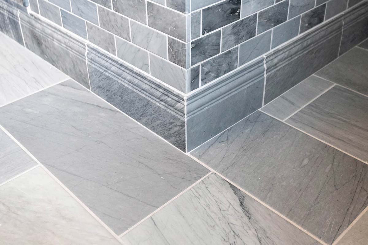 Stylish bathroom floor and wall with gray marble tiles and elegant baseboard trim, offering a sleek, modern look.