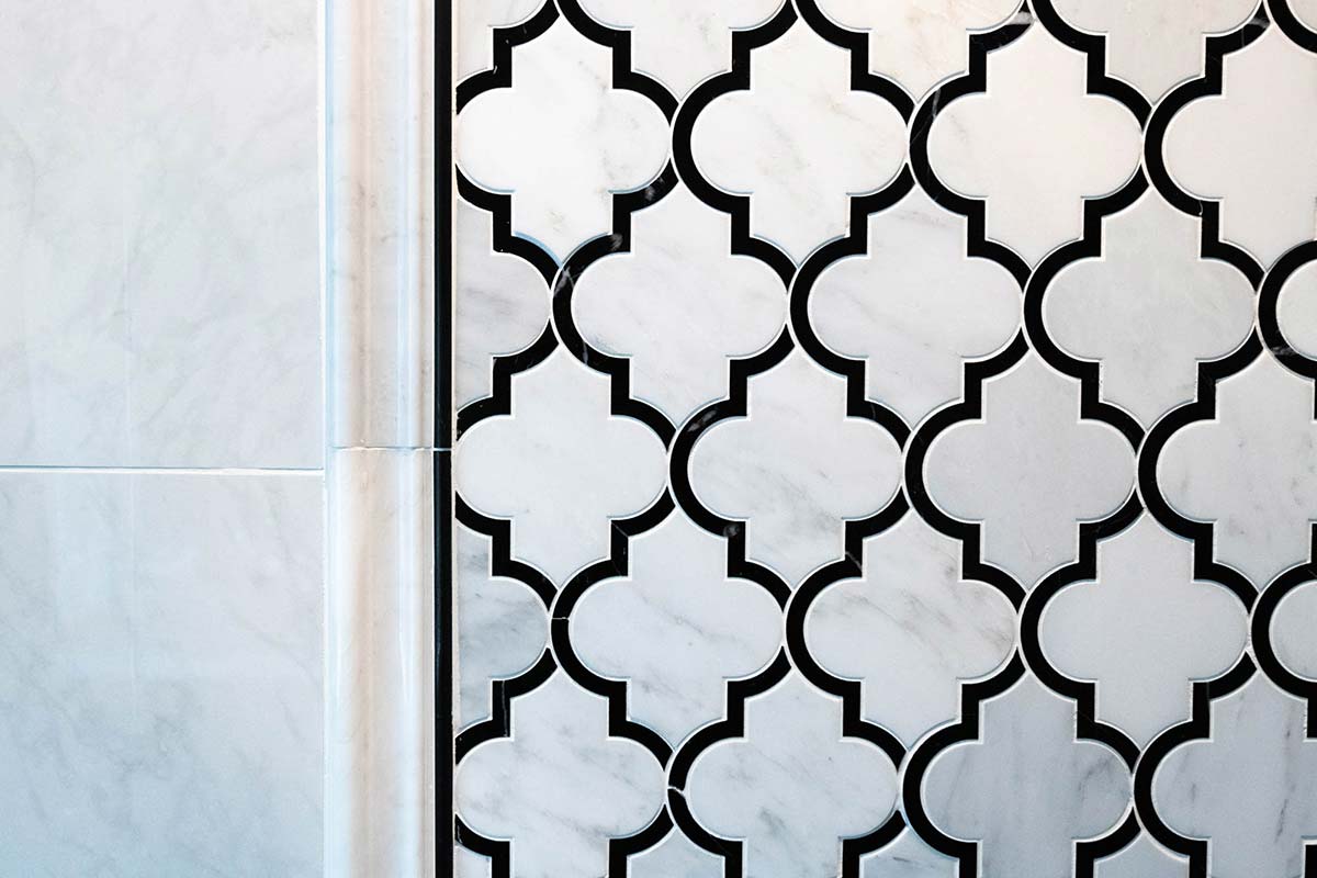 Elegant bathroom wall with white marble arabesque tiles and black accents, paired with smooth marble base.