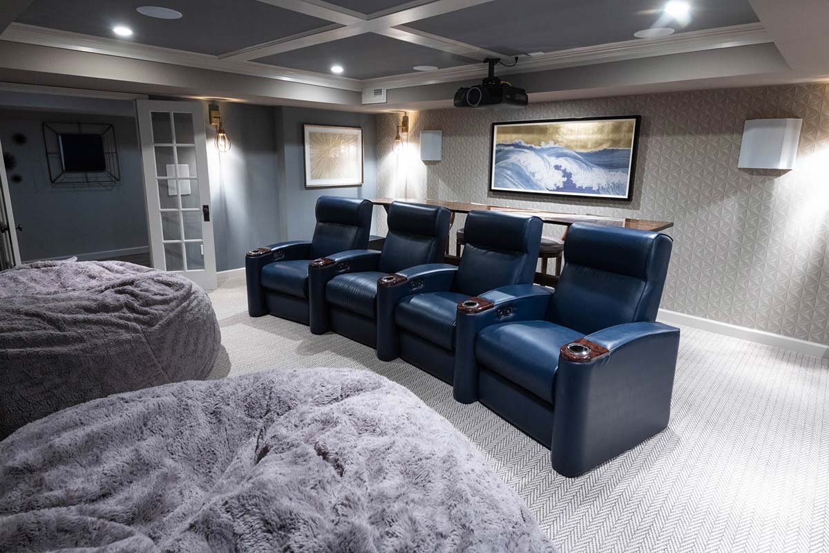 Cozy home theater with blue leather recliners, projector, and ocean artwork. Features bean bags and modern lighting.