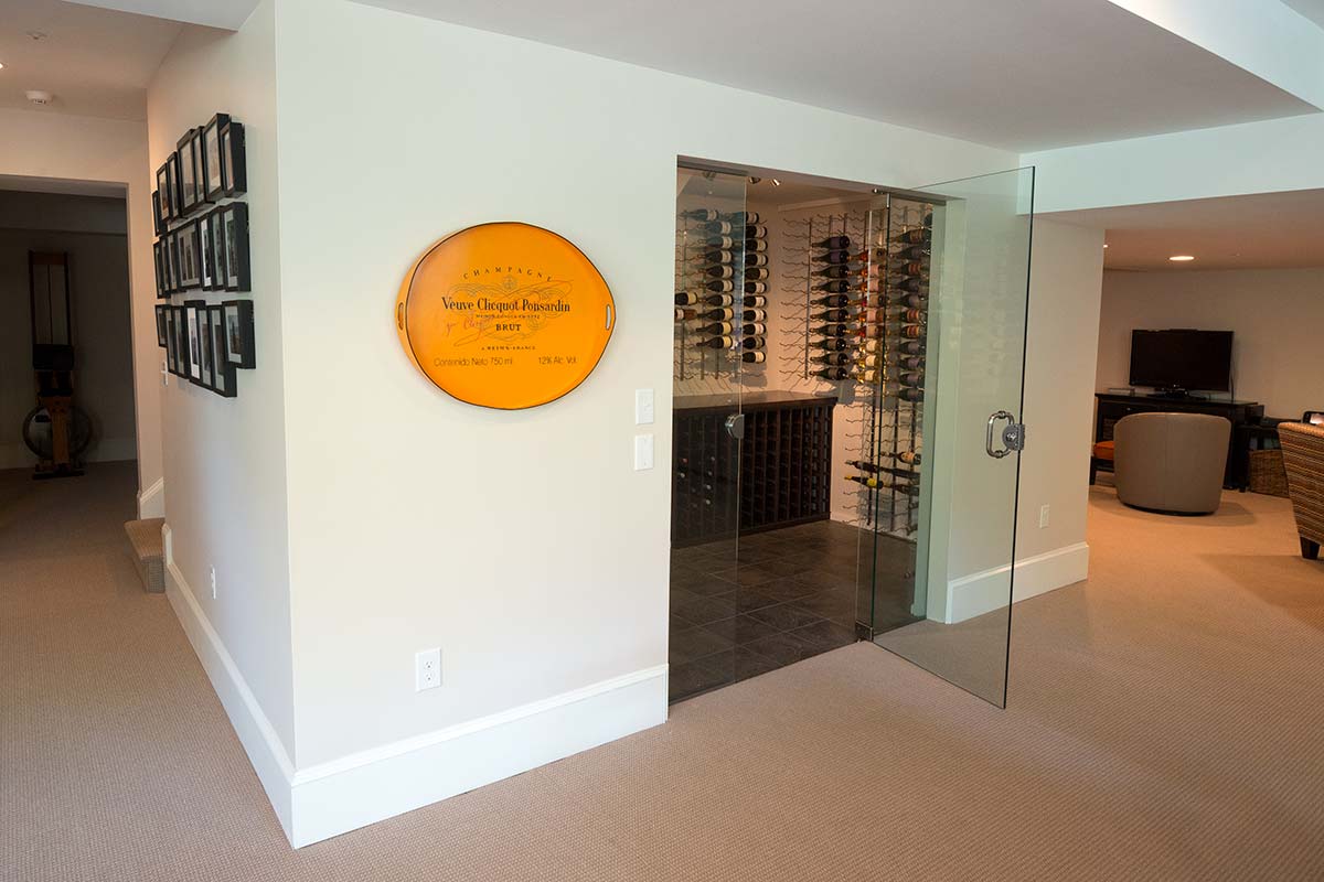 Stylish wine cellar with glass door, extensive bottle storage, and a decorative plaque, adjacent to a cozy living area.