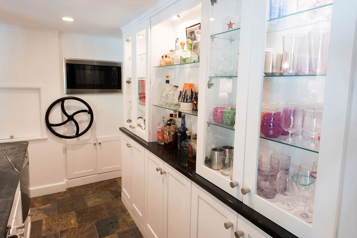 Modern bar cabinet with glass shelves, stocked with colorful bottles and glassware. Features a sleek black countertop and stylish decor accents.