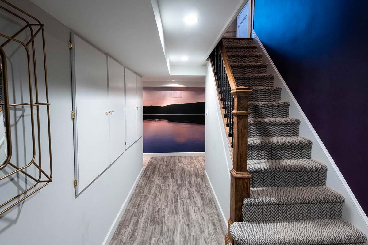 Stylish hallway with wooden flooring, a staircase with patterned carpet, and a scenic lake mural at the end.