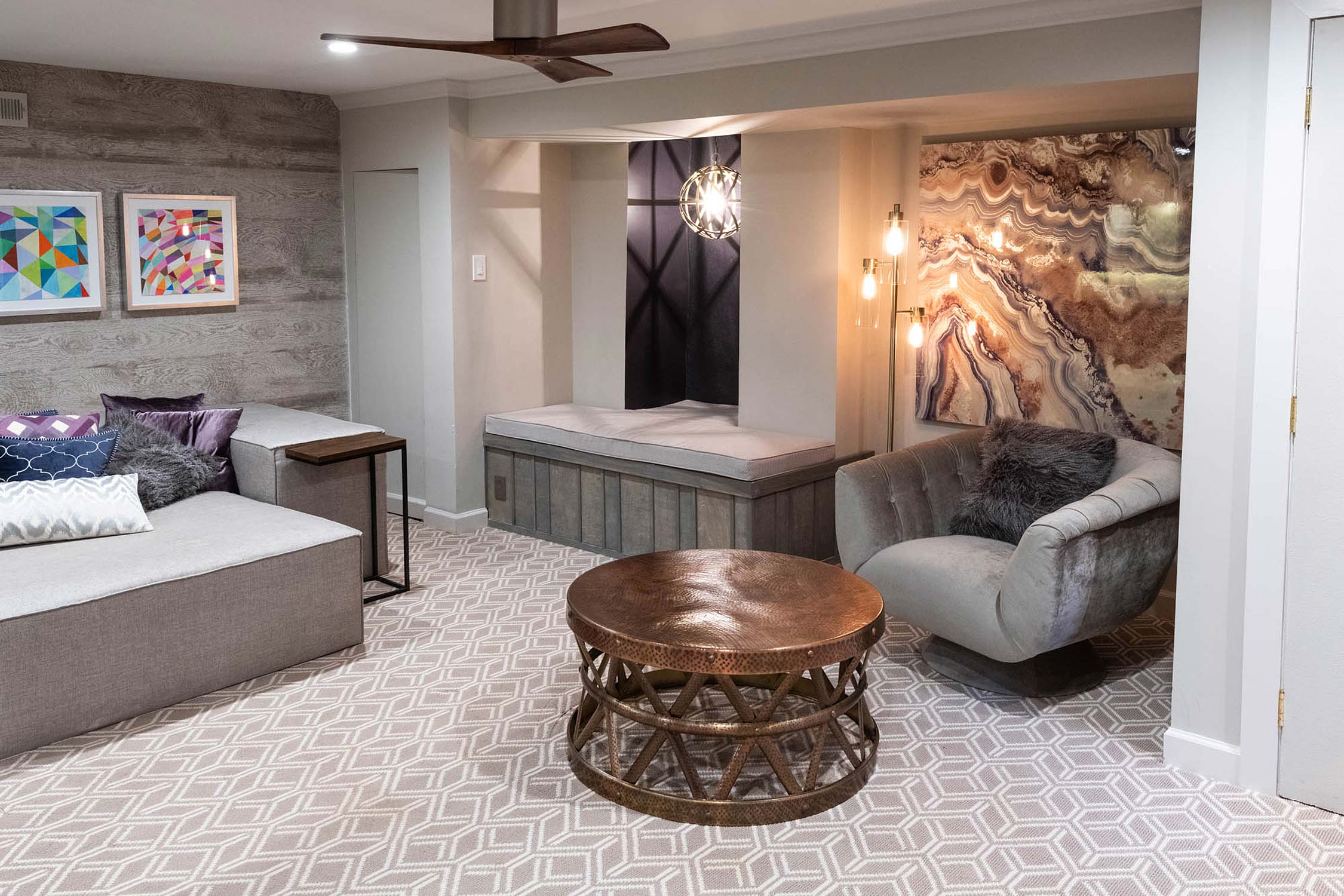 Modern sitting area with neutral tones, sectional sofa, copper table, swivel chair, and abstract artwork. Includes ceiling fan and patterned carpet.