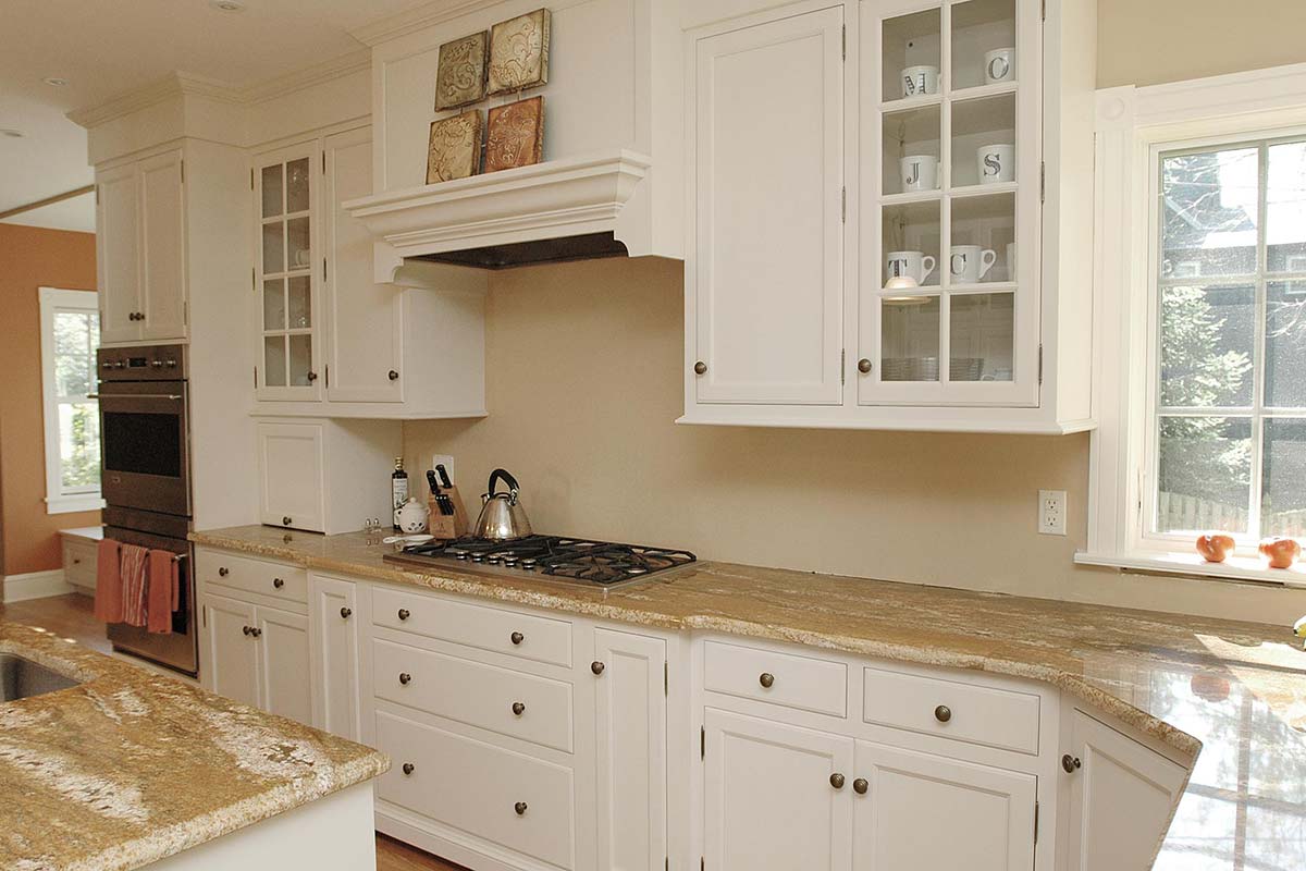 Bright kitchen with white cabinets, granite countertops, gas stove, and glassware display. Features natural light and modern appliances.