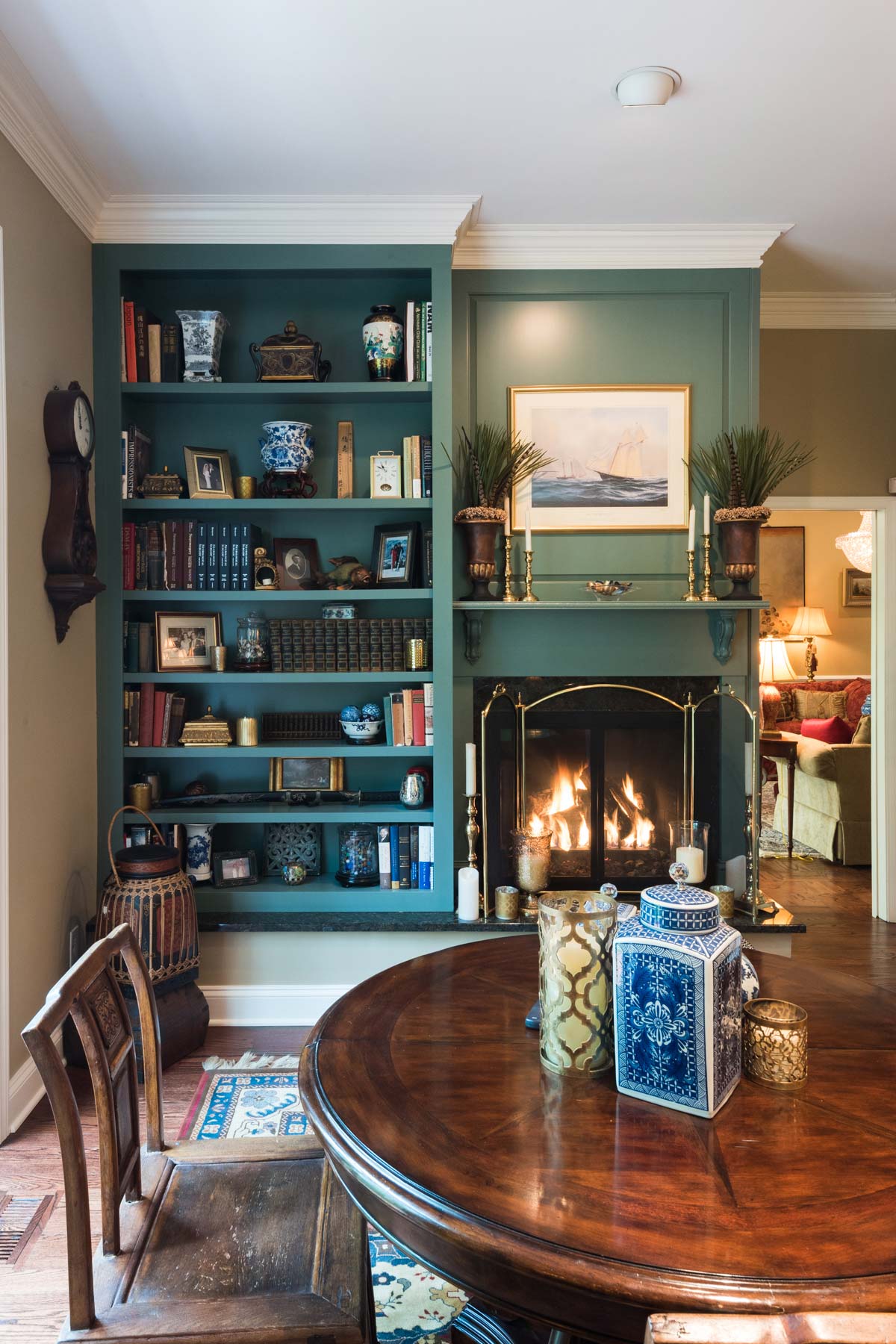 Cozy living room with a teal bookshelf filled with books, vases, and photos, a warm fireplace, and a polished wooden table with decorative jars.