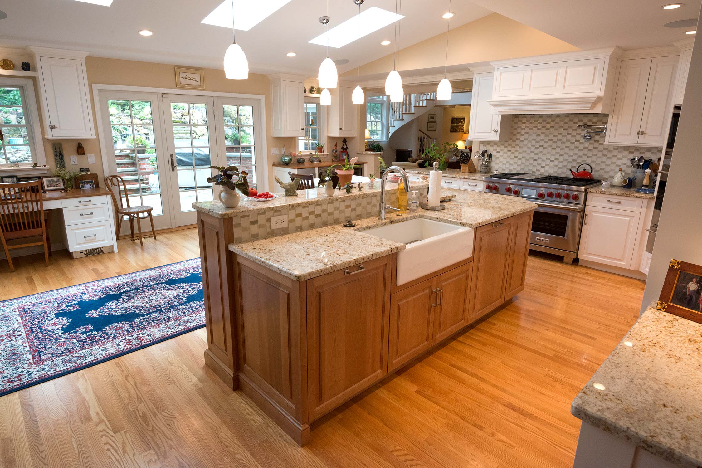 Bright kitchen with large island, granite countertops, and pendant lights. Features hardwood floors, white cabinets, tiled backsplash, and garden-view French doors.
