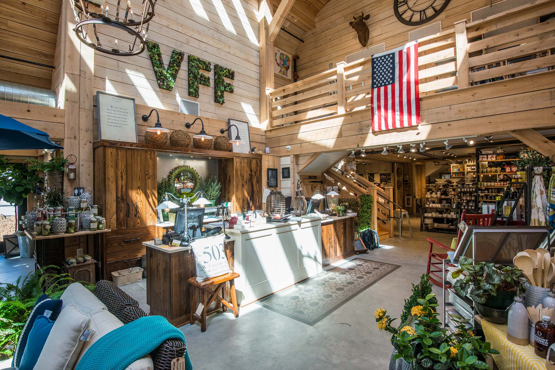 Wooden barn interior with VFF sign, American flag, chandelier, counter, plants, pillows, and decor items.