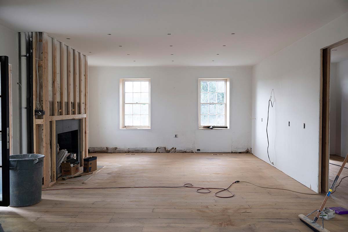 Interior room under construction with a window, framing lumber, insulation, and tools, lit by natural light.