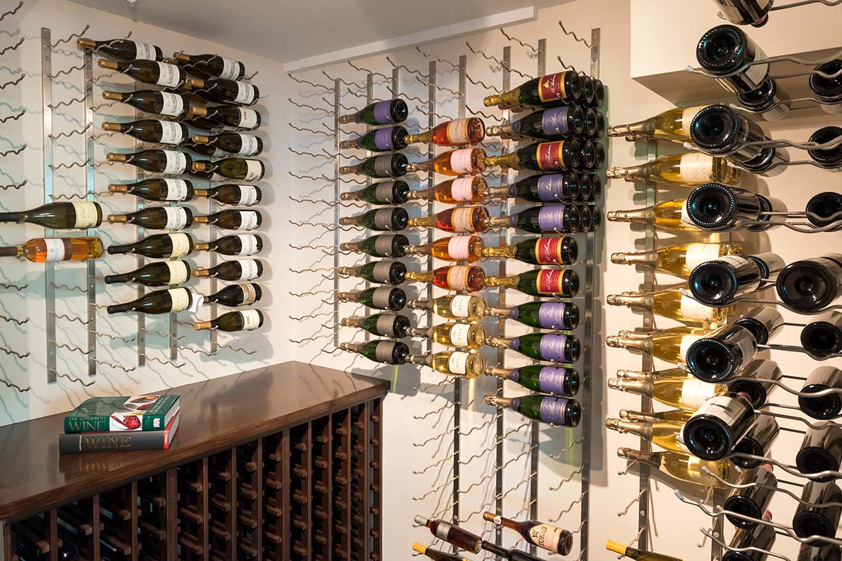 A stylish wine cellar with neatly arranged bottles on modern metal racks, featuring a variety of labels and colors, alongside a wooden cabinet and a wine book.