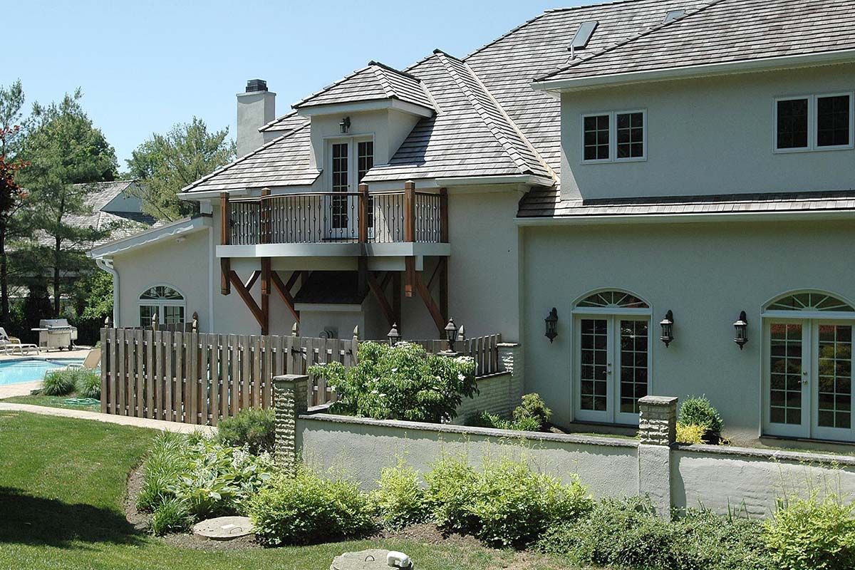 Modern home with a balcony, large windows, and lush garden, featuring a pool and wooden fence in a serene backyard setting.