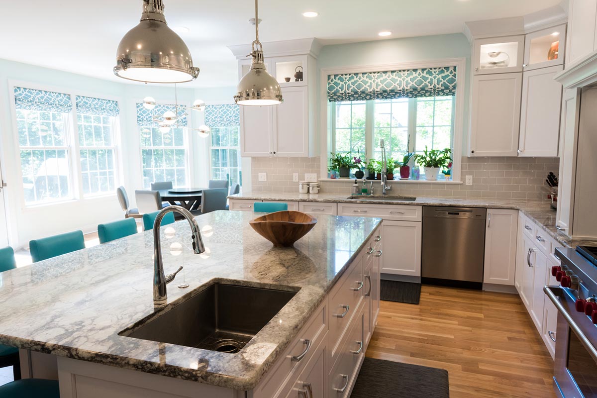 Modern kitchen with white cabinets, granite island, stainless steel sink, and turquoise stools. Features large windows, pendant lights, and a dining area view.