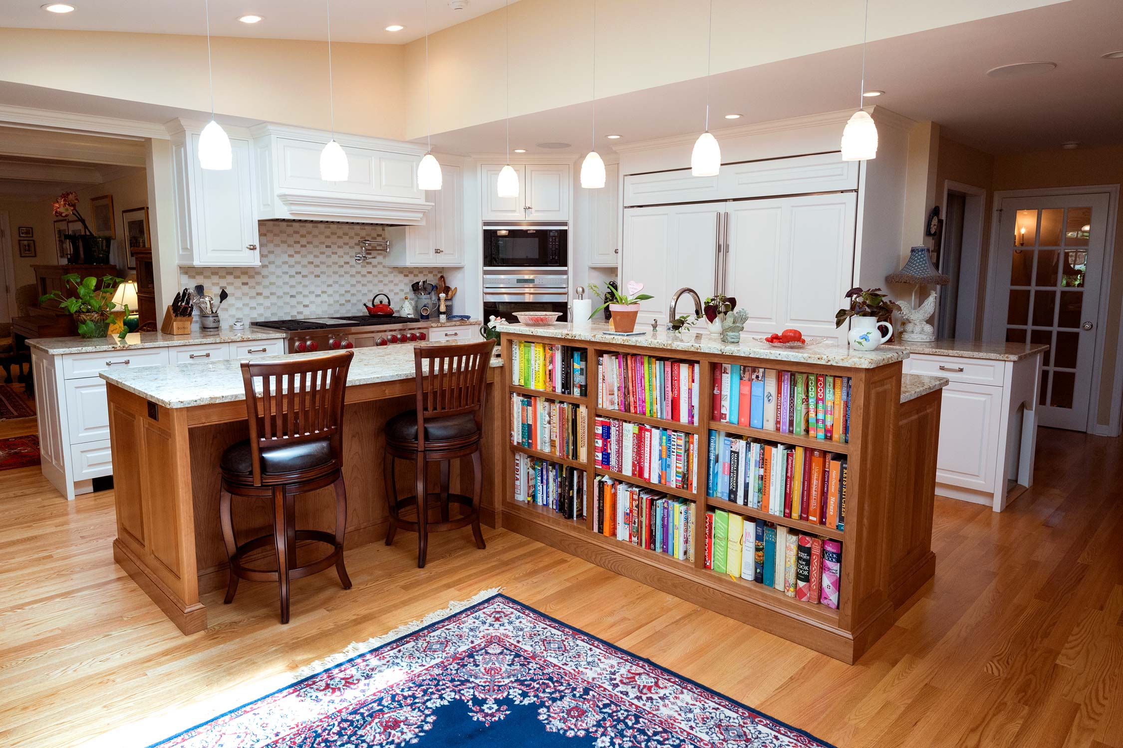 Modern kitchen with large island, built-in bookshelves, and pendant lights. Features granite countertops, white cabinets, tiled backsplash, and hardwood floors.