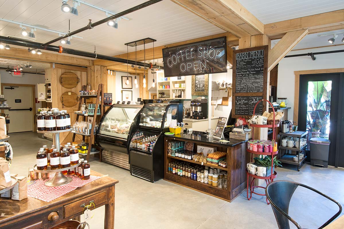 Rustic coffee shop with wooden beams, counter, chalkboard menu, bottled drinks, pastries, and decor items.