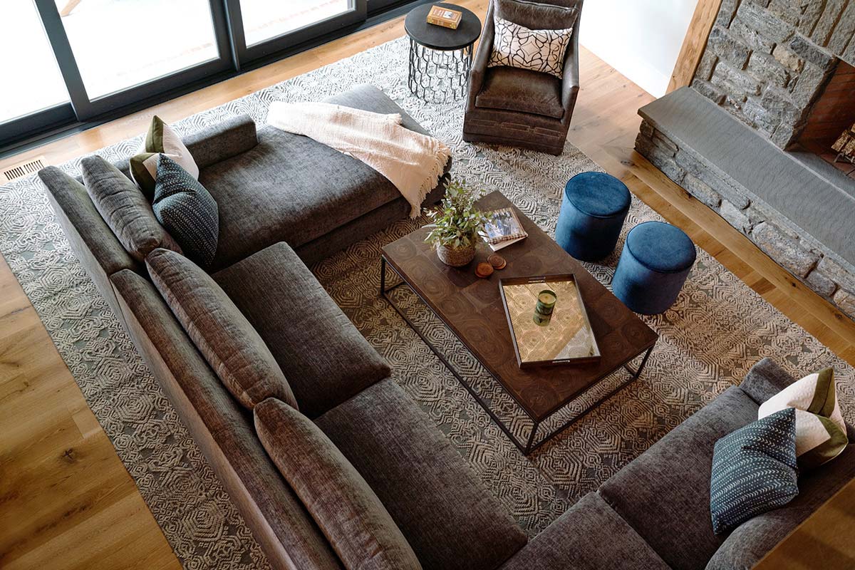 Cozy living room with a gray sectional sofa, wooden coffee table, blue ottomans, and a stone fireplace, viewed from above.