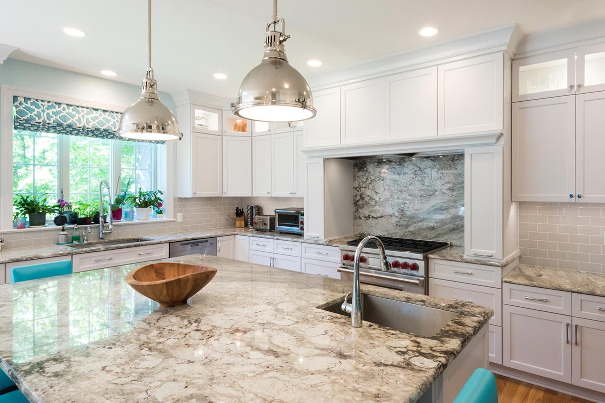 Bright kitchen with white cabinets, granite island, stainless steel sink, and turquoise stools. Features pendant lights, large windows, and a stylish range.