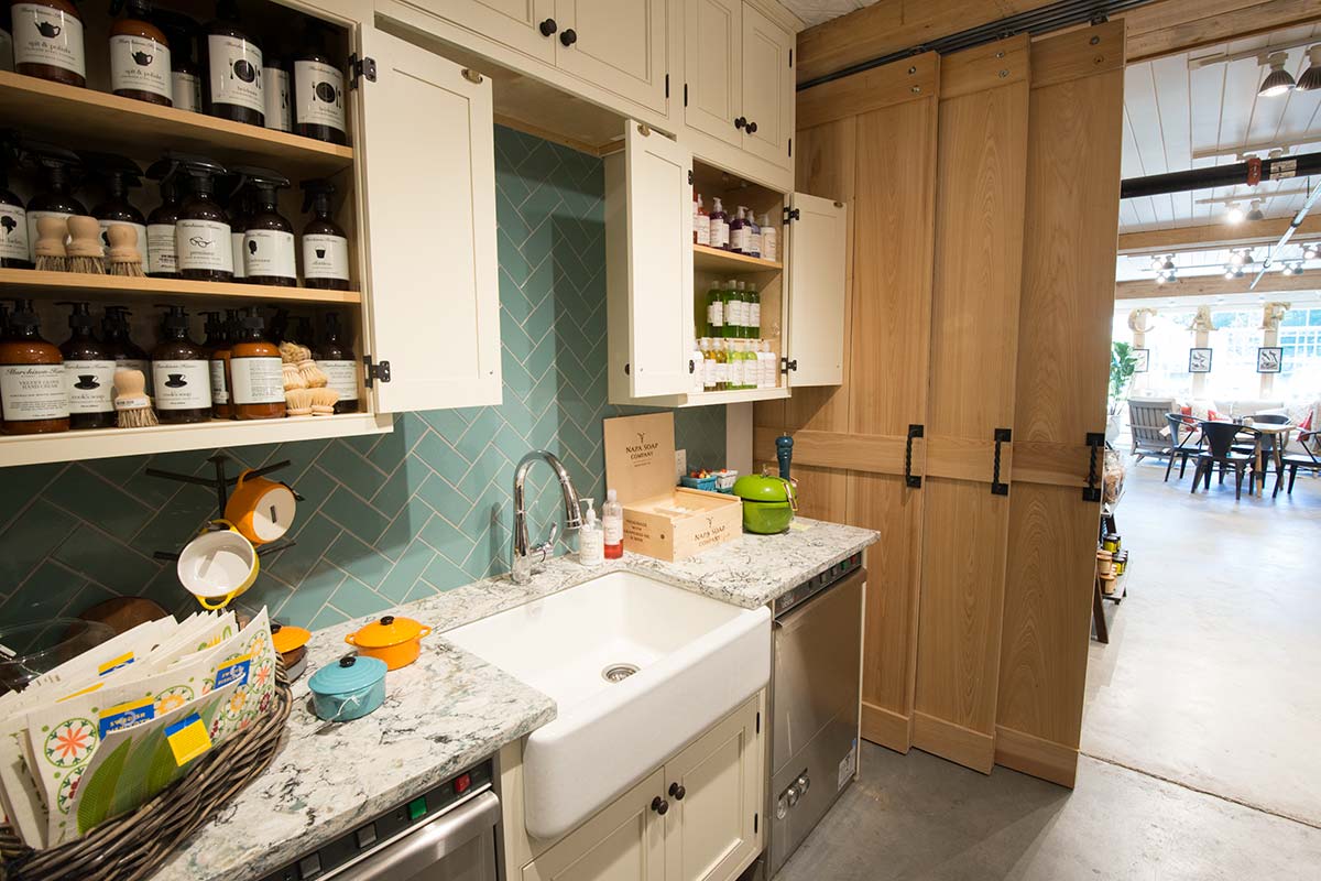 Farmhouse kitchen with white cabinets, blue backsplash, farmhouse sink, and wooden sliding doors, filled with cleaning products.