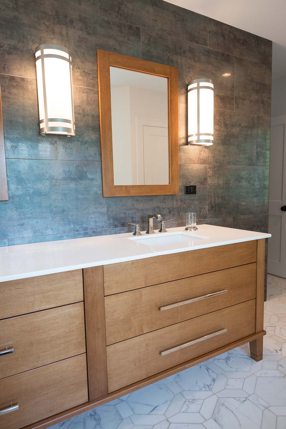 Sleek bathroom with dual sinks, wooden vanity, gray tile wall, and elegant marble hexagon floor.