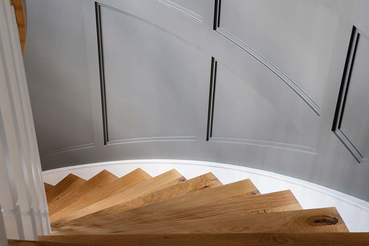 Curved wooden staircase with white balusters, set against a gray paneled wall, viewed from a top-down perspective.