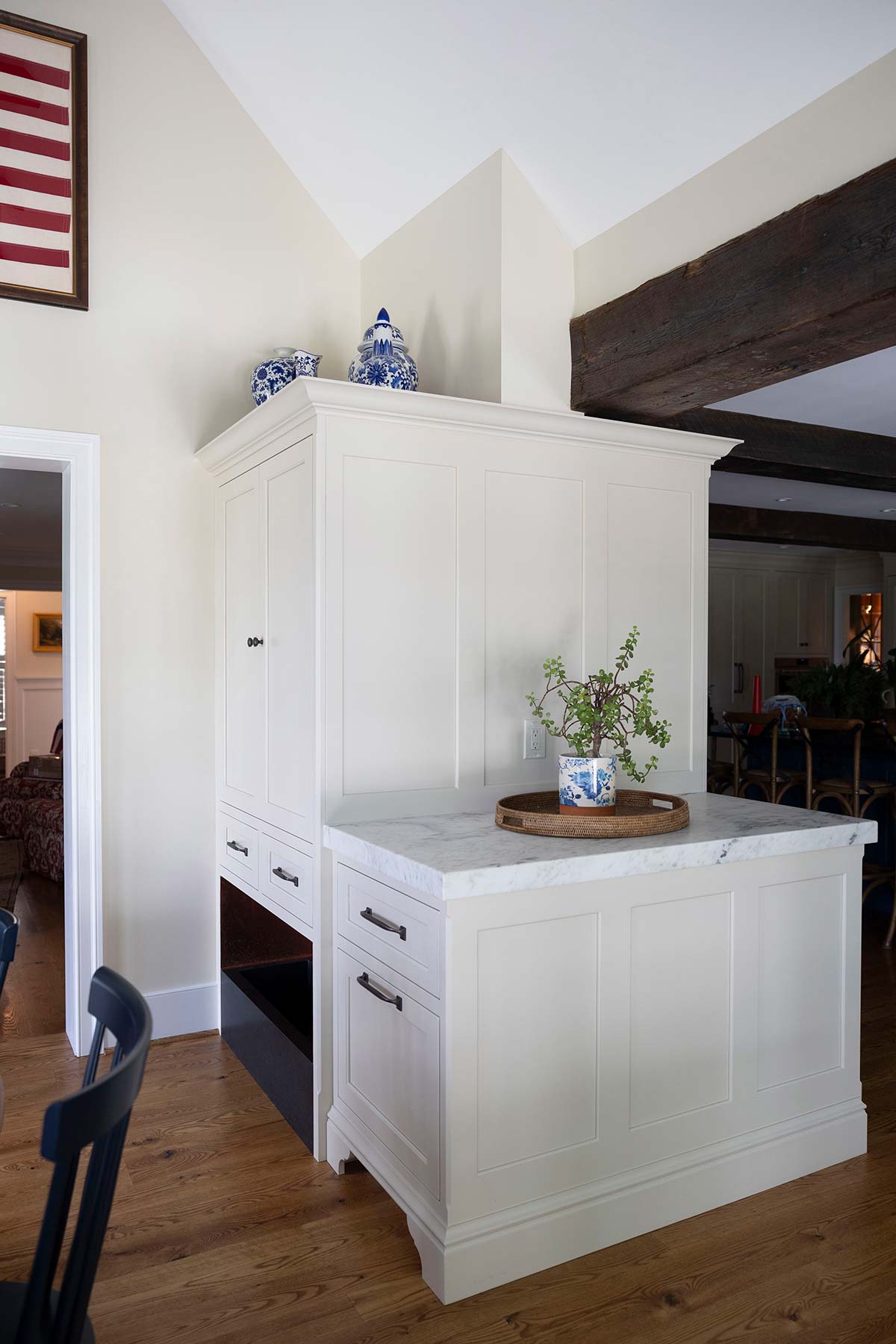 Elegant kitchen island with white cabinetry, marble countertop, and decorative blue-and-white pottery, accented by wooden beams and flooring.