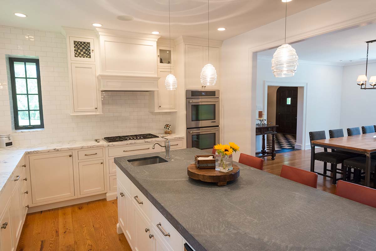 Modern kitchen with white cabinets, subway tile backsplash, double ovens, island, and dining area with wooden table.