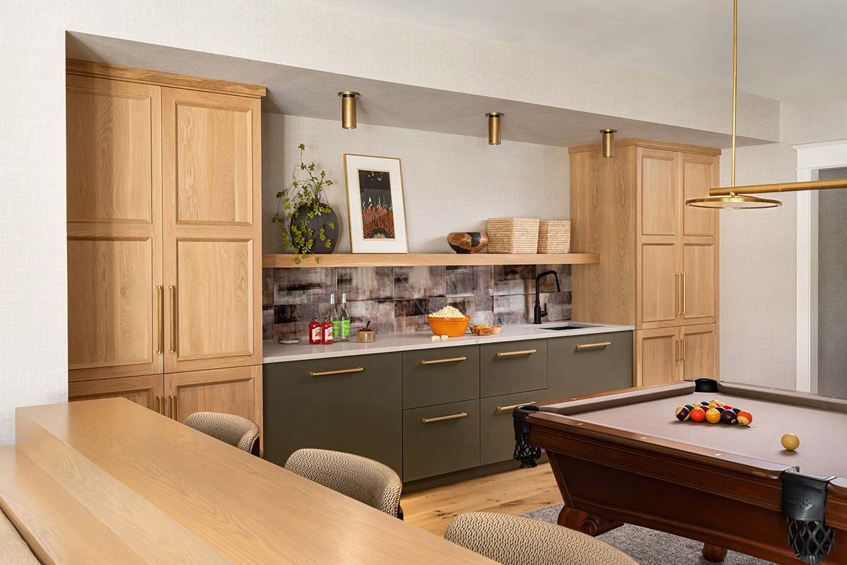 Modern kitchen with wooden cabinets, gray counter, and a pool table, featuring a gold pendant light and snacks on display.