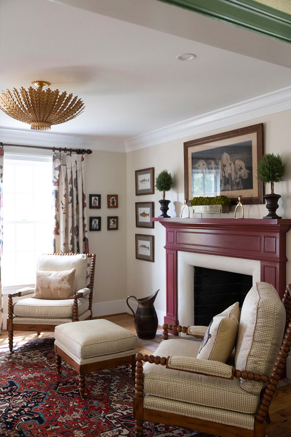 Cozy room with maroon fireplace, wooden chair, and ornate rug. Decor includes a painting, plants, and a horse figurine on the hearth.