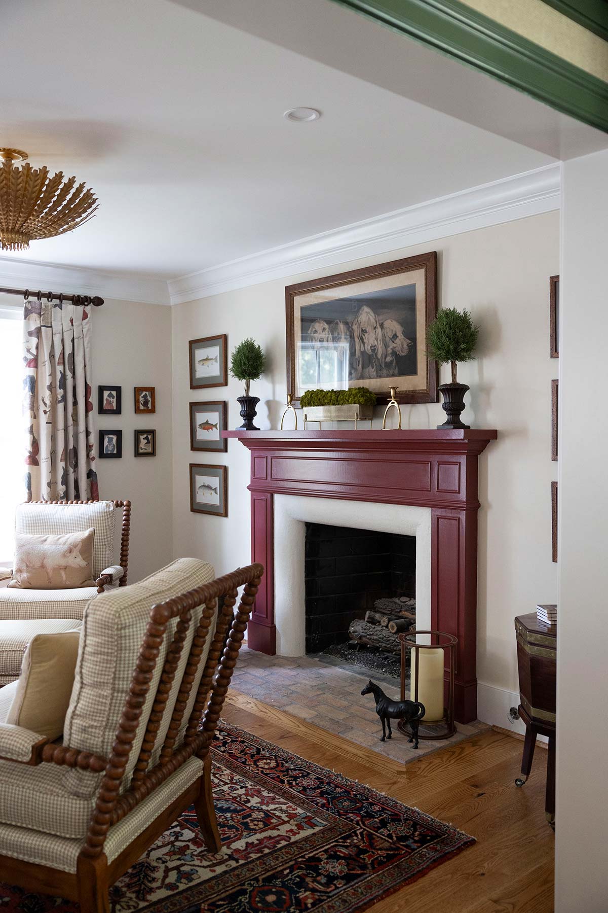 Cozy room with maroon fireplace, wooden chair, and ornate rug. Decor includes a painting, plants, and a horse figurine on the hearth.