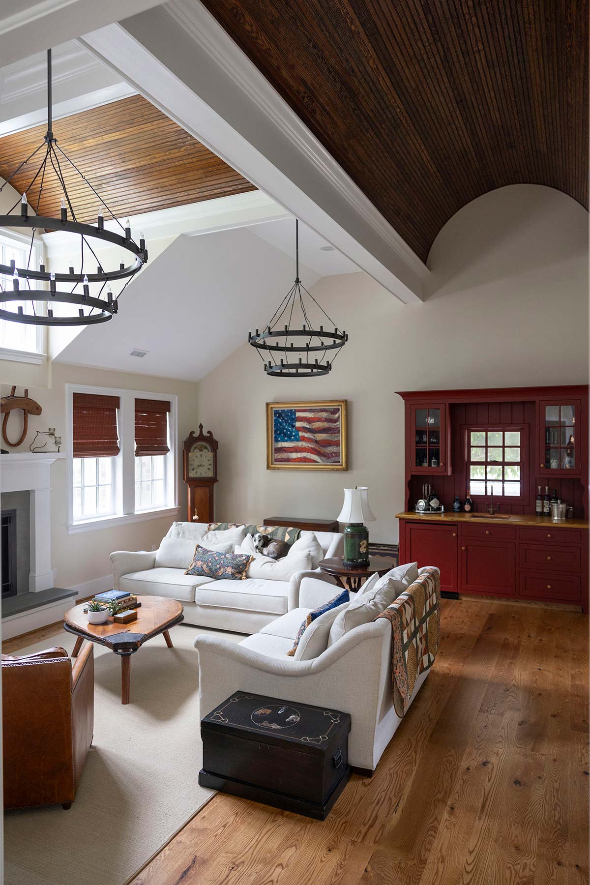 Cozy living room with white sofas, wooden coffee table, and red cabinet. Features a flag painting, chandelier, and fireplace with wood floor.