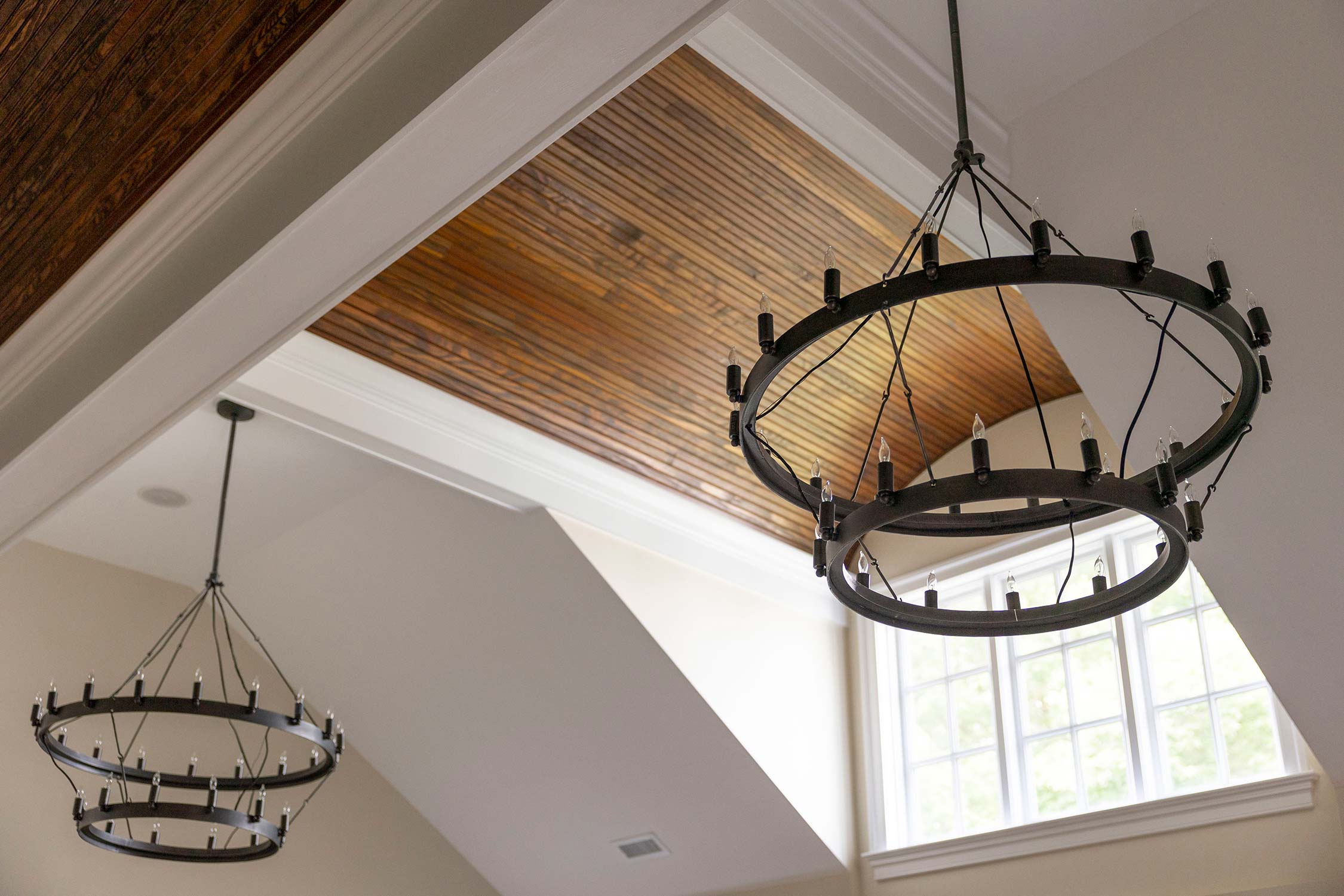 Elegant room with wooden ceiling and two black chandeliers. Large windows and white walls create a bright, airy atmosphere.