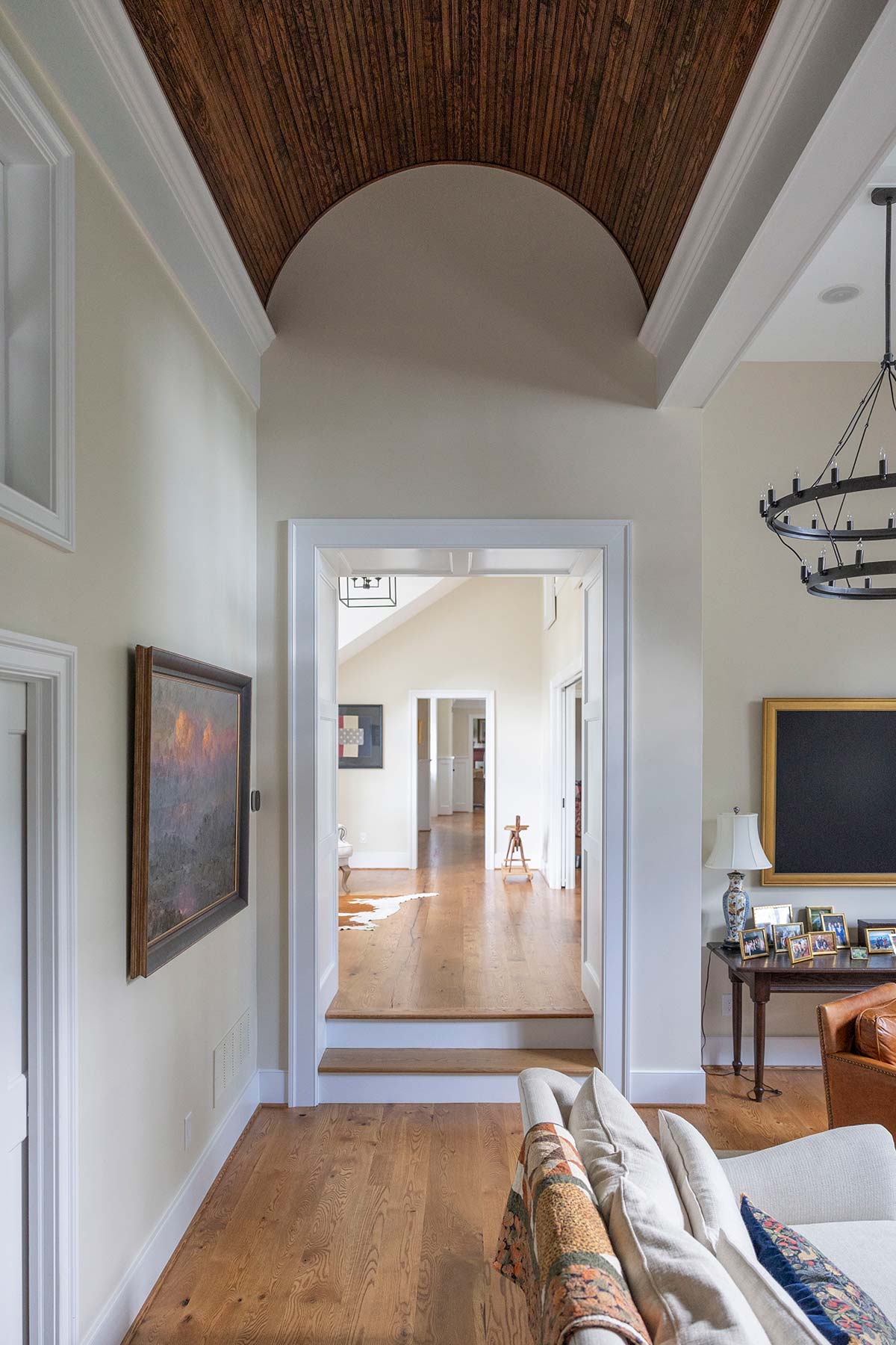 A stylish home interior with wooden floors, arched ceilings, artwork, and a cozy sofa, featuring a chandelier and open layout.
