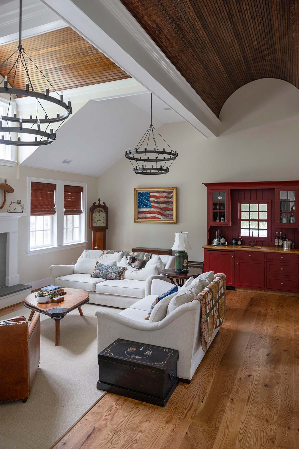 Cozy living room with white sofas, wooden coffee table, and red cabinet. Features a flag painting, chandelier, and fireplace with wood floor.