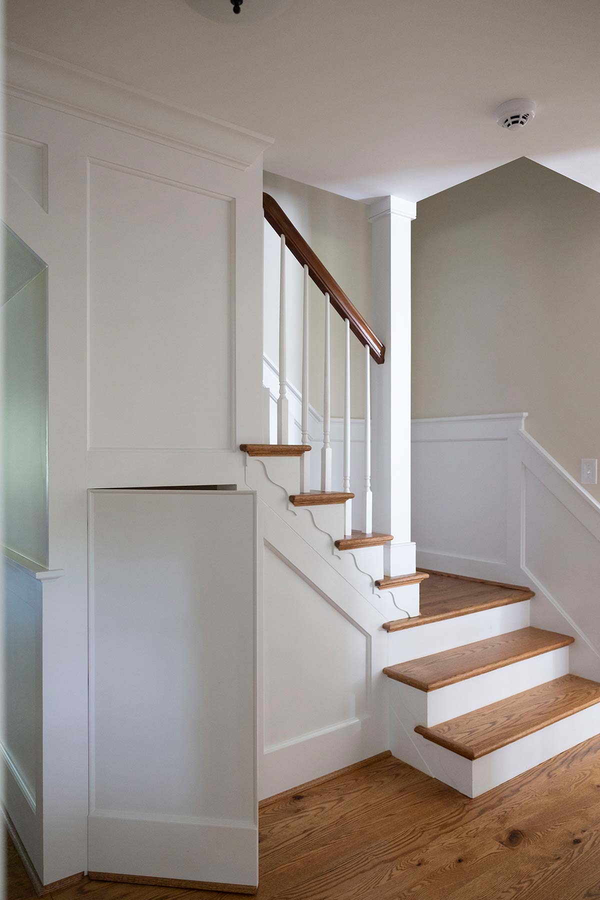 Elegant staircase with white railings, wooden steps, and a hidden door. Features wood flooring and neutral walls with a modern design.
