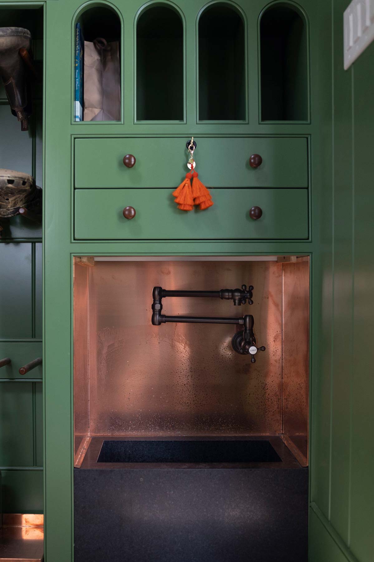 A stylish green cabinet with arched shelves, drawers, a copper sink, and a modern faucet, accented by an orange tassel.