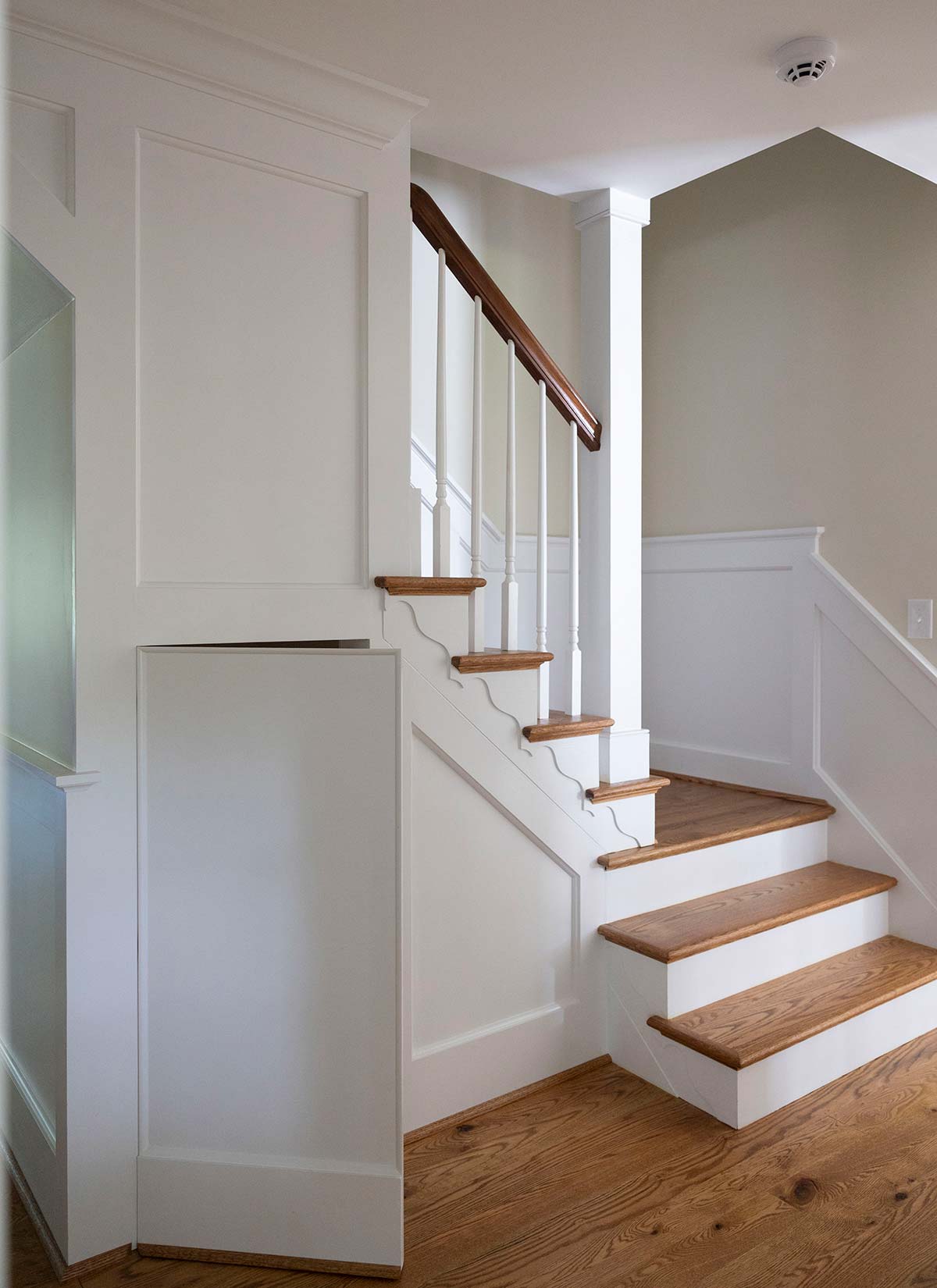 Elegant staircase with white railings, wooden steps, and a hidden door. Features wood flooring and neutral walls with a modern design.