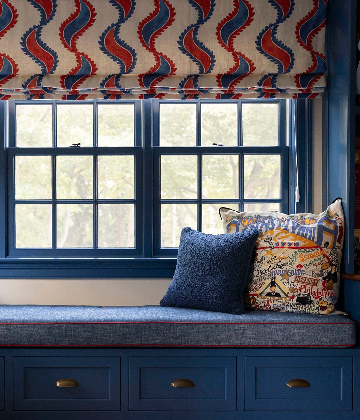 A cozy window nook with a blue bench, vibrant curtains, and decorative pillows, offering a perfect reading spot.