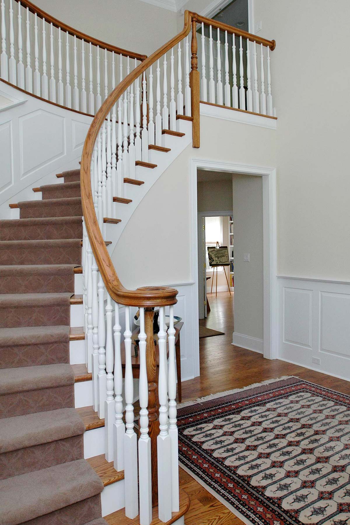 Elegant curved staircase with white balusters, wooden handrail, and a patterned rug in a bright, spacious foyer.