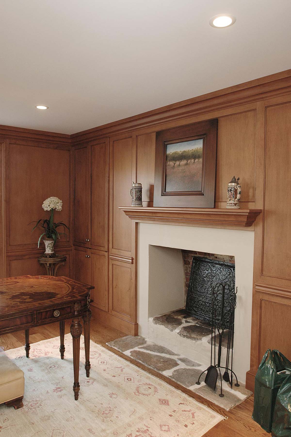 Cozy room with wooden paneling, a fireplace, and a wooden table, decorated with flowers and art on a patterned rug.