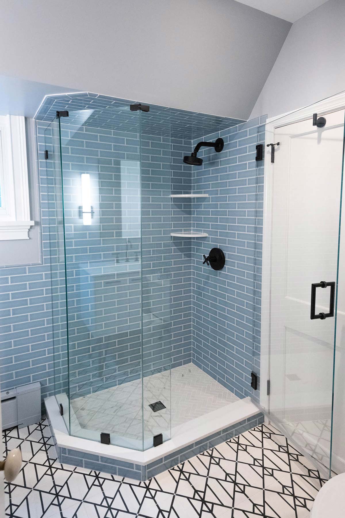 Stylish bathroom with a glass shower, blue subway tiles, and geometric floor tiles, featuring modern lighting and a sleek design.