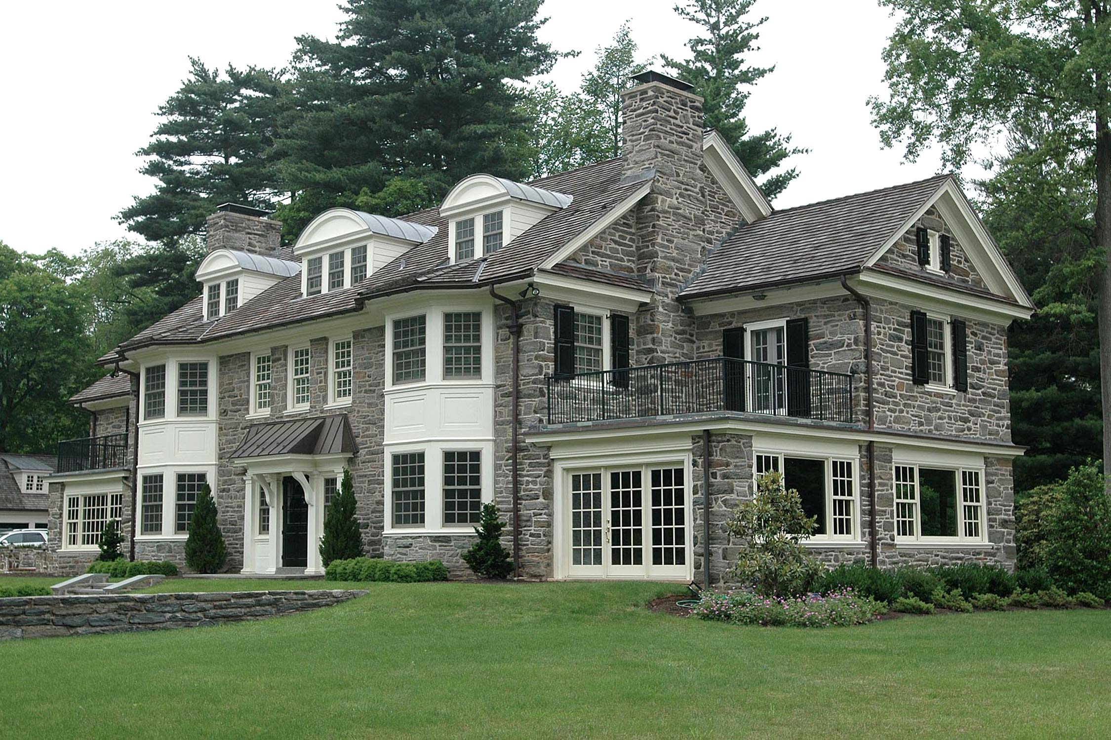 Elegant stone mansion with large windows and a balcony, nestled among lush trees and greenery.