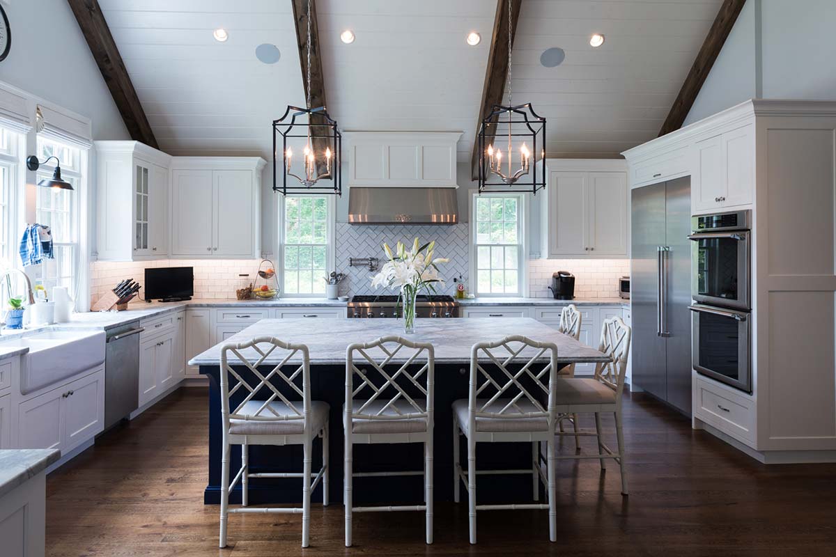 Spacious modern kitchen with white cabinets, vaulted ceiling, and elegant island seating, accented by fresh flowers.