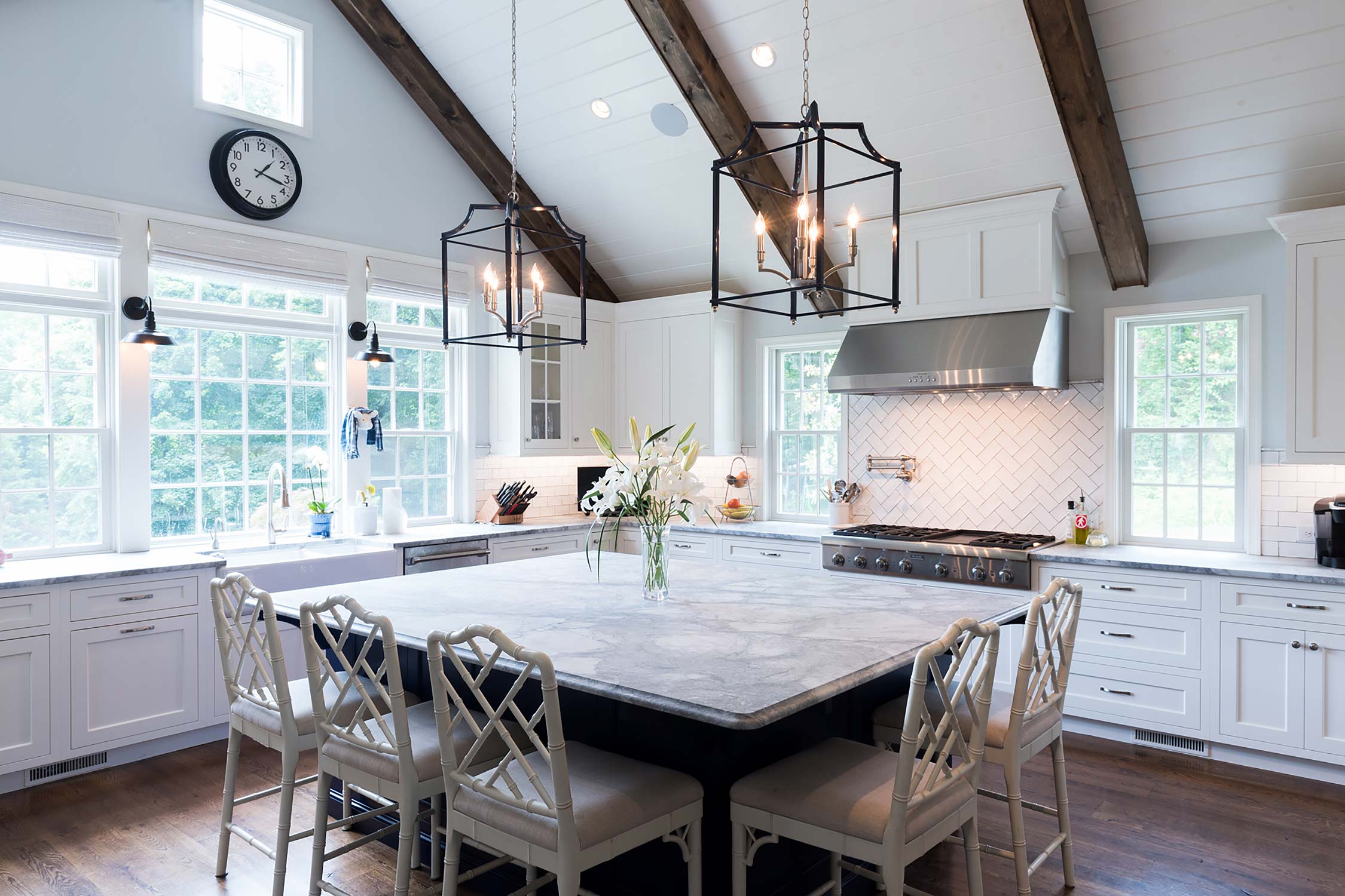 Bright modern kitchen with vaulted ceiling, white cabinets, and a spacious island with stylish chairs and flowers.